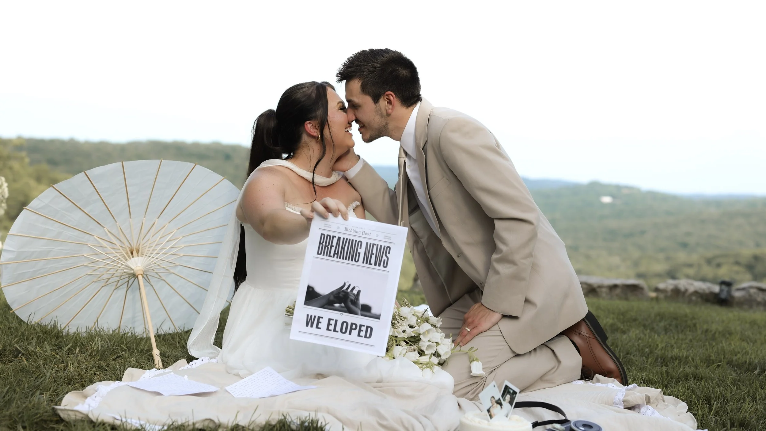 Black and white photo of a bride and groom touching noses, smiling, with a wedding banner in the background.