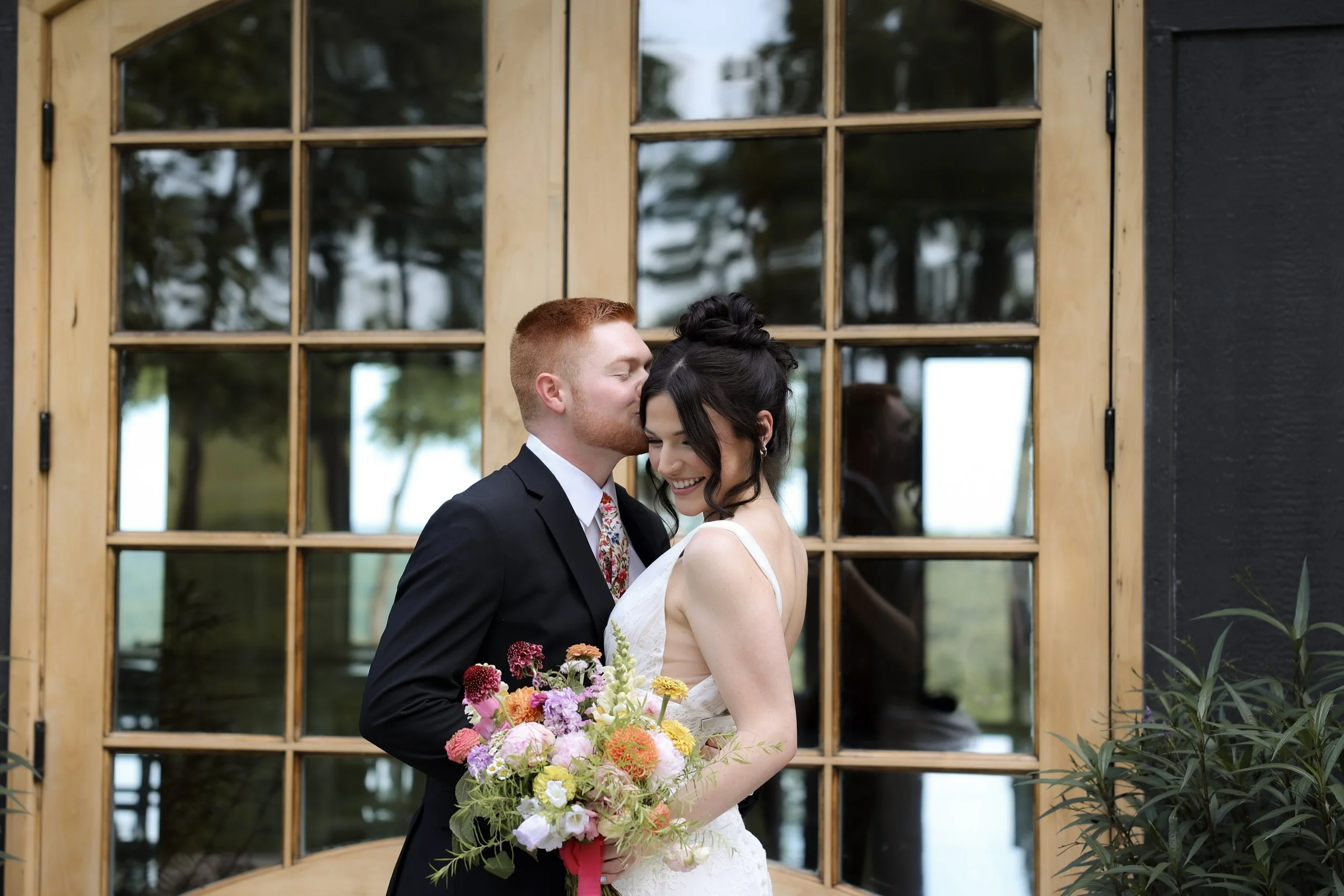 Group of people in wedding attire celebrating and sharing a joyful moment outdoors, with a bride and groom at the center.
