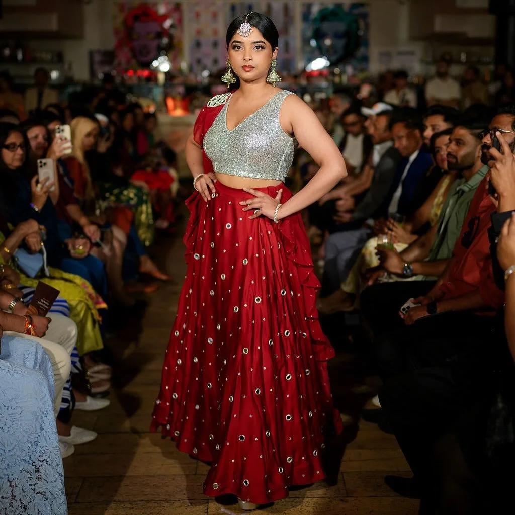 A symphony of shimmer and tradition — the Sindoori Ensemble embodies bold elegance with every detail. The gleaming silver blouse meets a richly embroidered scarlet lehenga, where hand-done mirror work and cascading ruffles create a mesmerizing