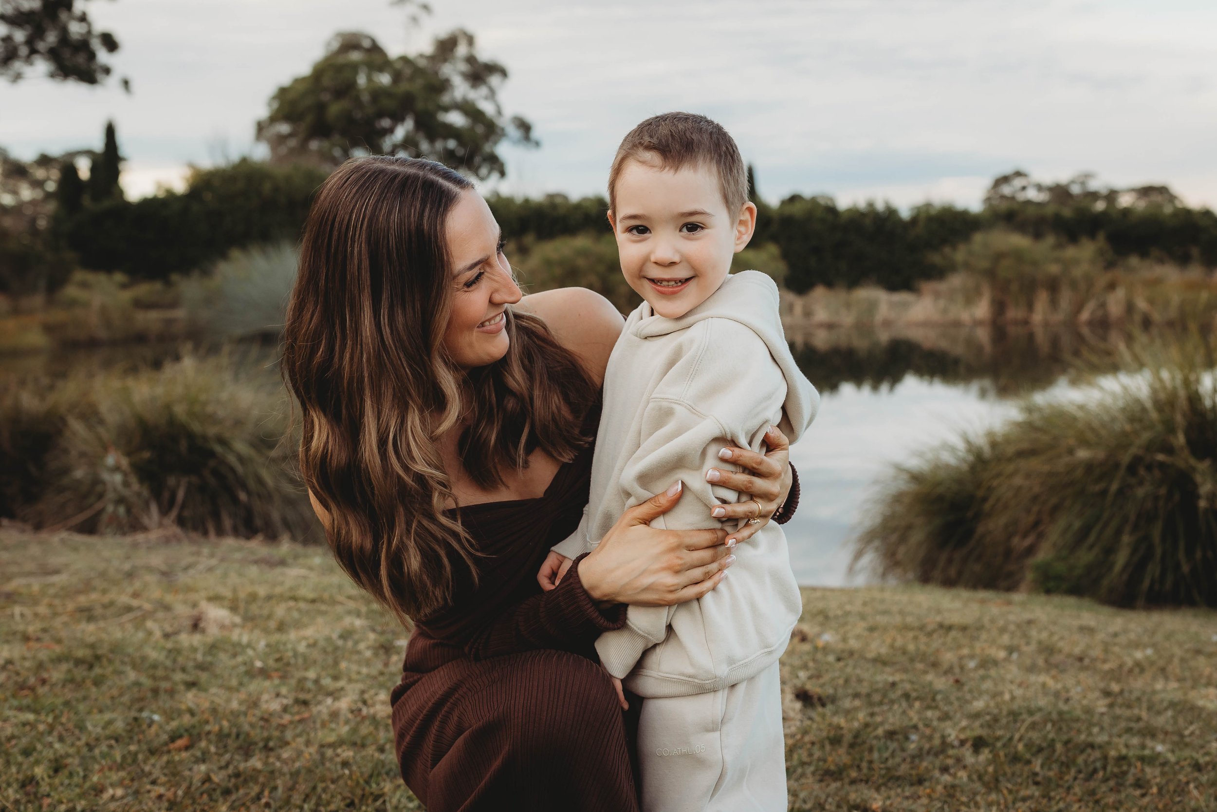 Mother and child in a family photoshoot wearing warm jumpers and dresses in front of a water feature at their home