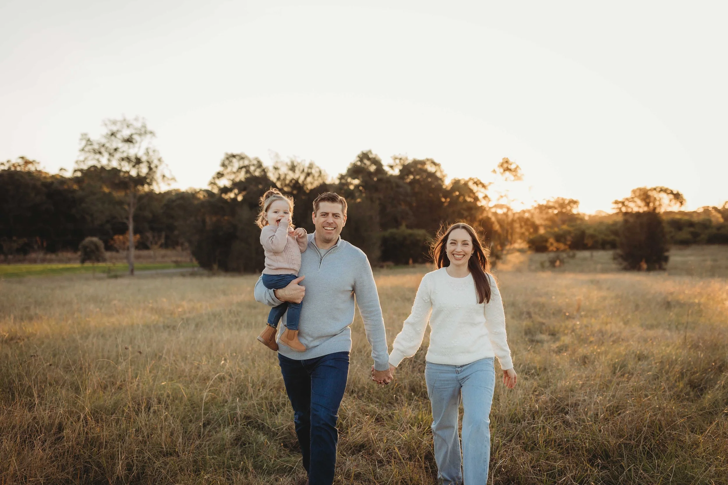 Three people walking in a field wearing knitted jumpers and jeans at golden hour sunset