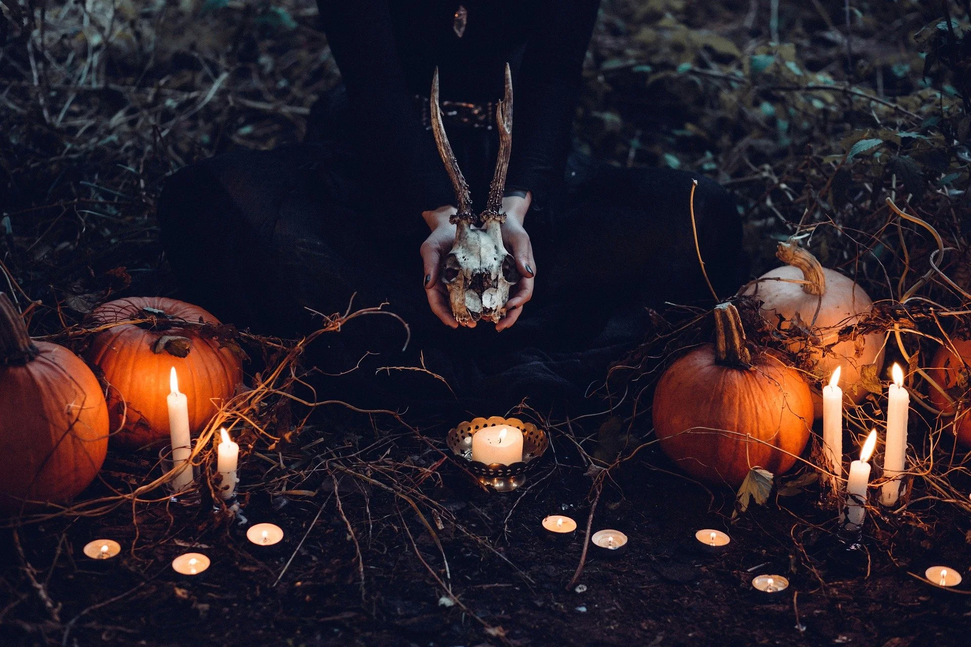 headless witch holding a goat skull surrounded by pumpkins and candles