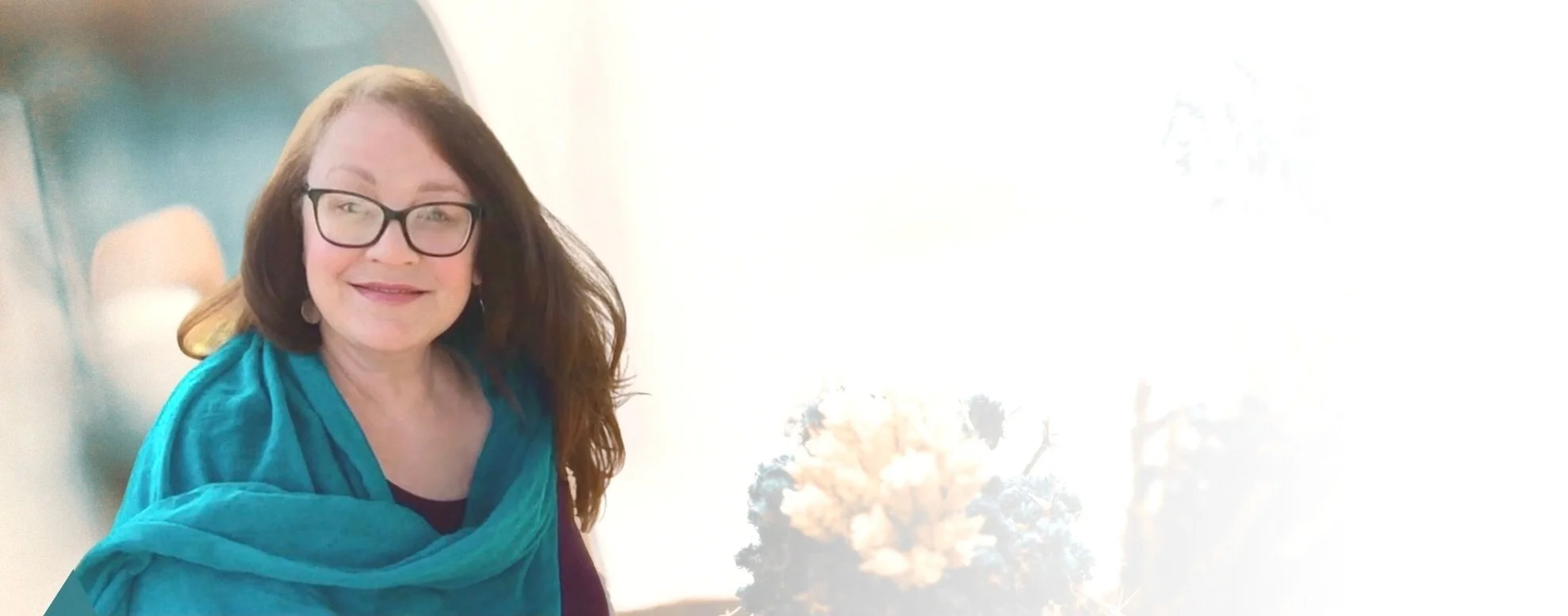 Victoria Maxwell-Davis, wearing a teal shawl, looks to camera against an out of focus teal and golden background.