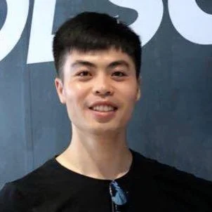 Smiling man in front of a sign with partial letters visible