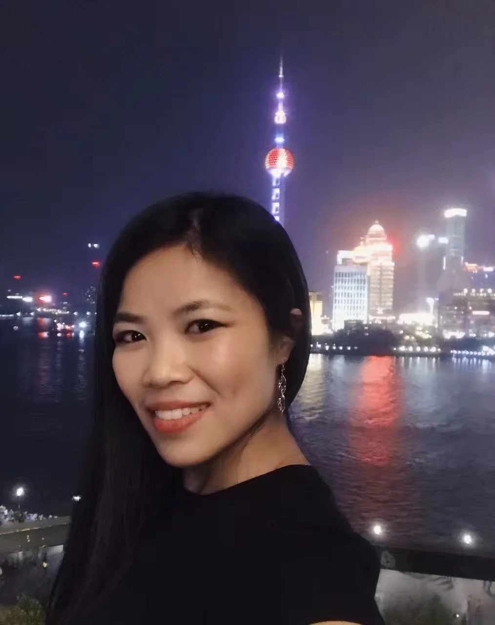 Woman taking a selfie at night with Shanghai skyline and Oriental Pearl Tower in the background.