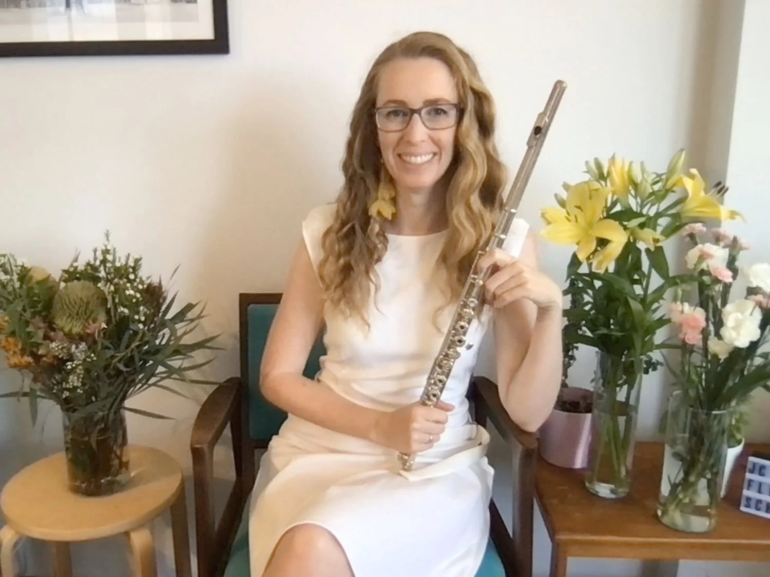 Jane Cavanagh smiling and holding a flute. She has blonde hair and she is wearing glasses and a white dress