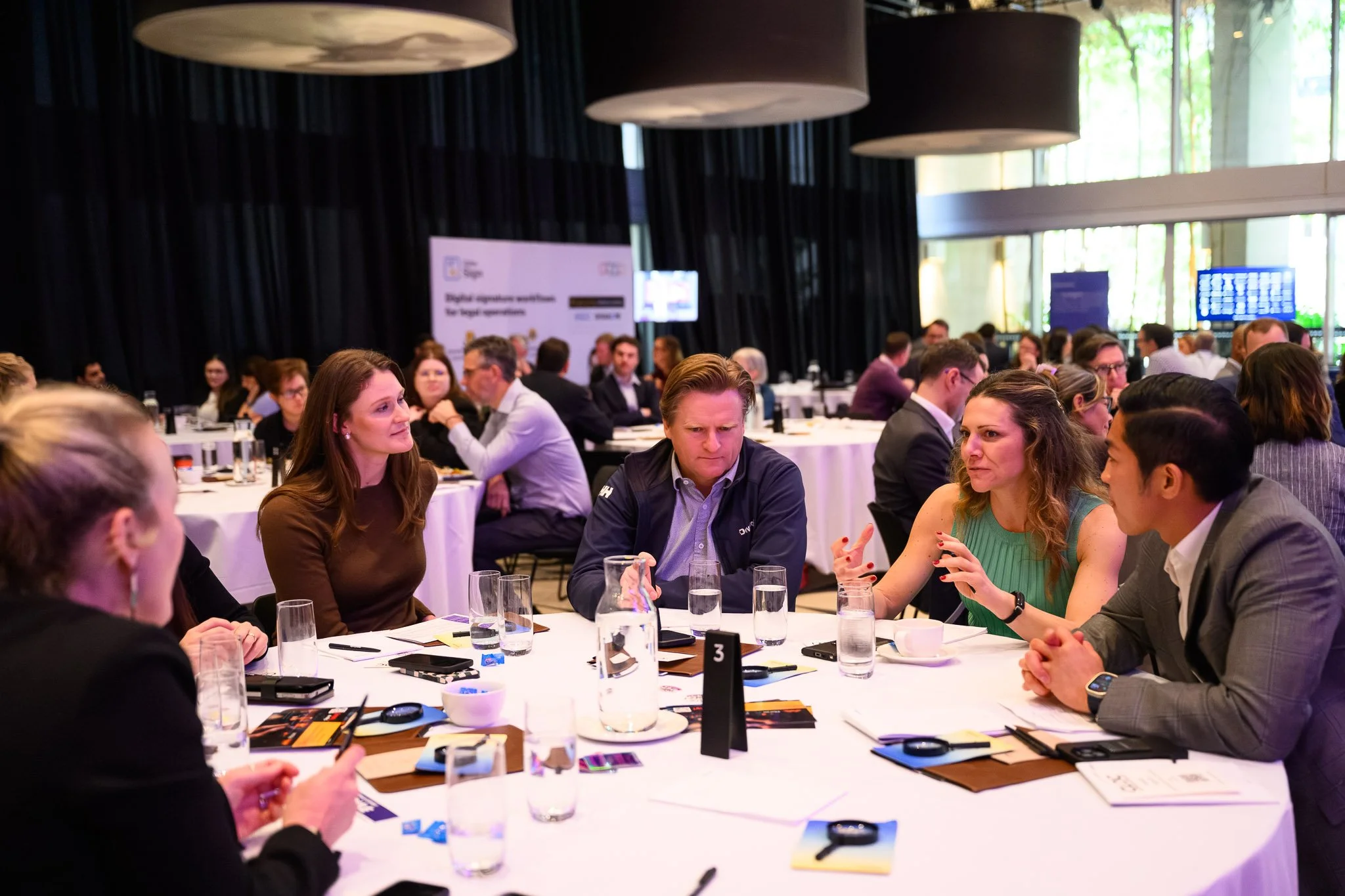 Verity white smiling and sitting in front of a print that reads "Rebels get results". She is wearing a black jacket, white top and blue jeans