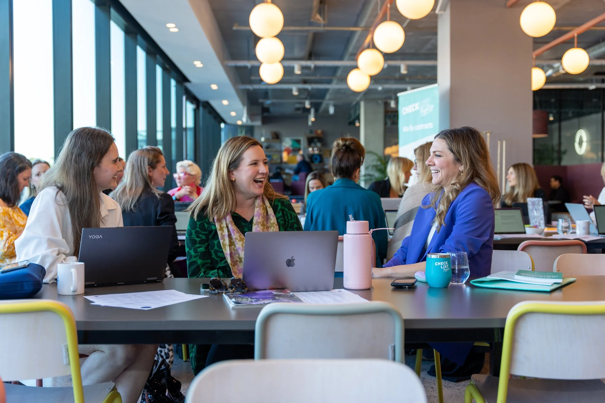 Verity laughing while talking to another woman. Verity is wearing a yellow jacket and black top and pants
