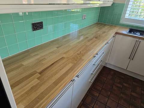 A long view of a fully restored oak kitchen worktop featuring a smooth, dry matte hardwax oil protective coating near a sink.
