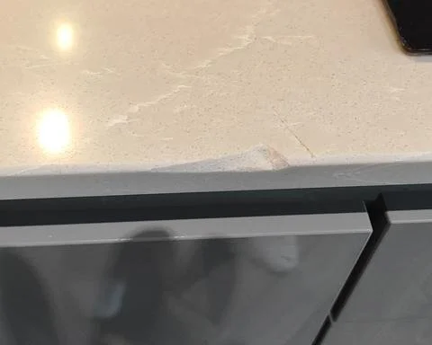 A large chip damage on the edge of a veined beige quartz kitchen worktop before professional stone repair in Guildford.