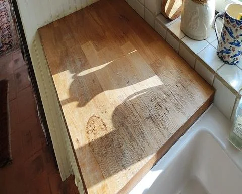 Water damaged oak kitchen worktop with black ring stains and deep scoring next to a Belfast sink.