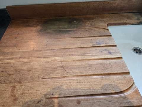 A worn wooden kitchen worktop next to a white sink showing a deep black burn mark caused by a hot cooking pan.