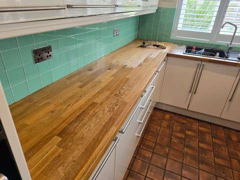 A Purdy heavy-duty hand scraper resting on an oak worktop where sticky oil buildup is being shaved away down to bare wood.