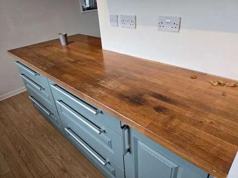 A tacky, sticky wooden kitchen island worktop surface showing uneven shiny spots and gummy residue from failed Danish oil.