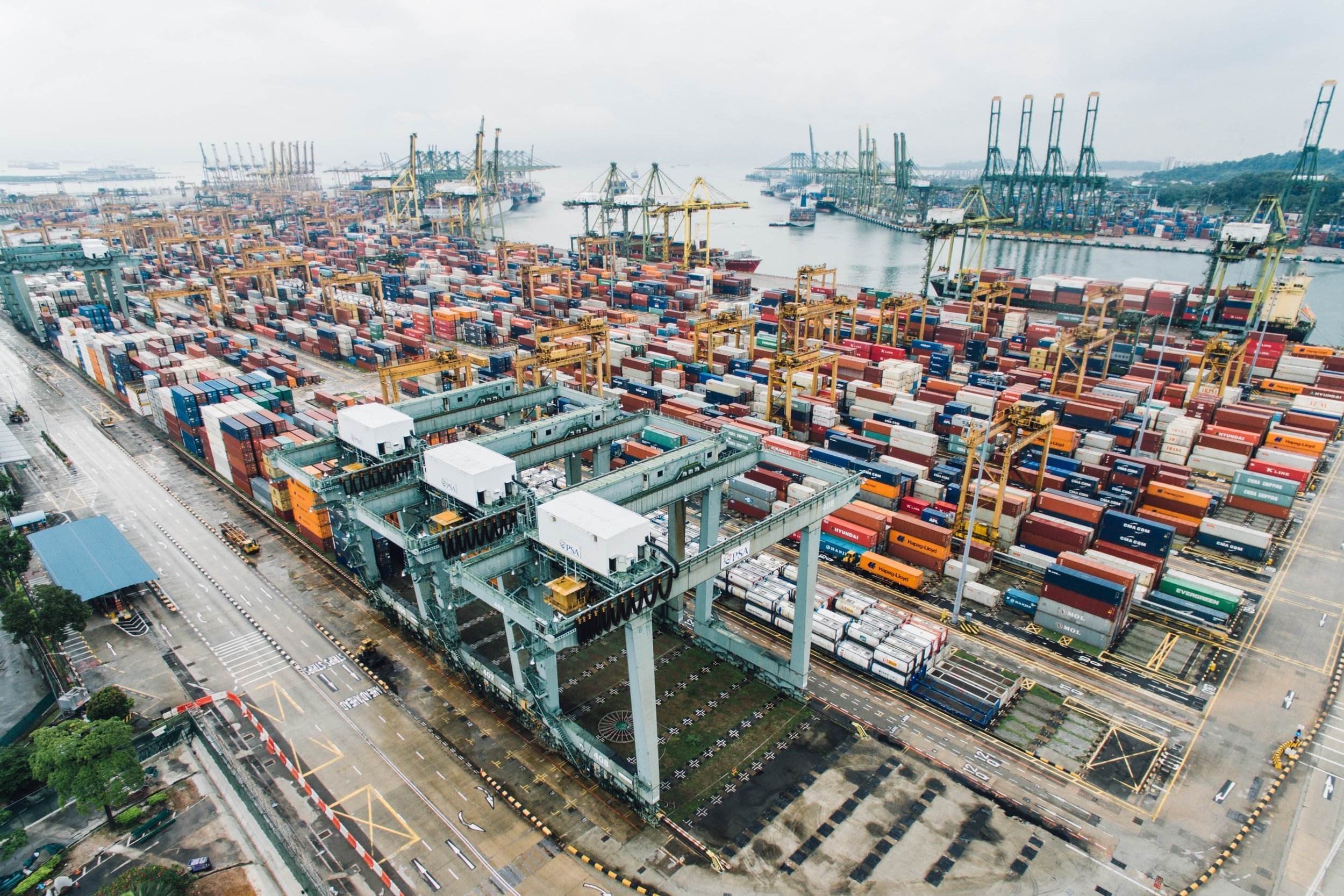 A large container yard by the water, with cranes in the background, seen from above