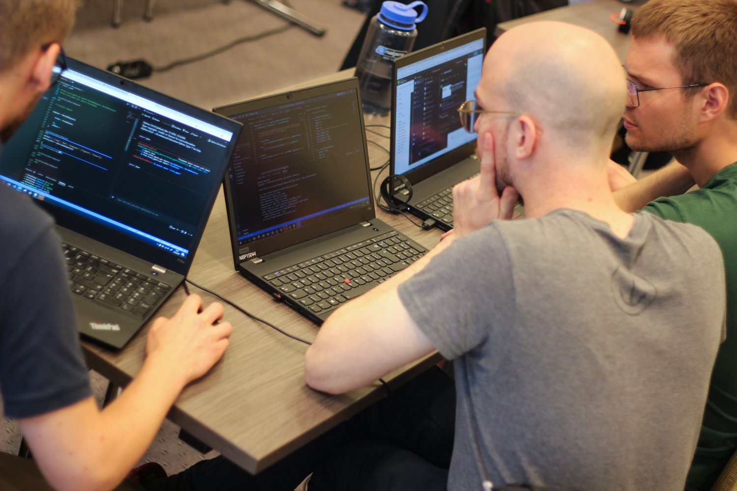 3 hackathon attendees seen from the back as they sit huddled together at their laptops, looking concentrated