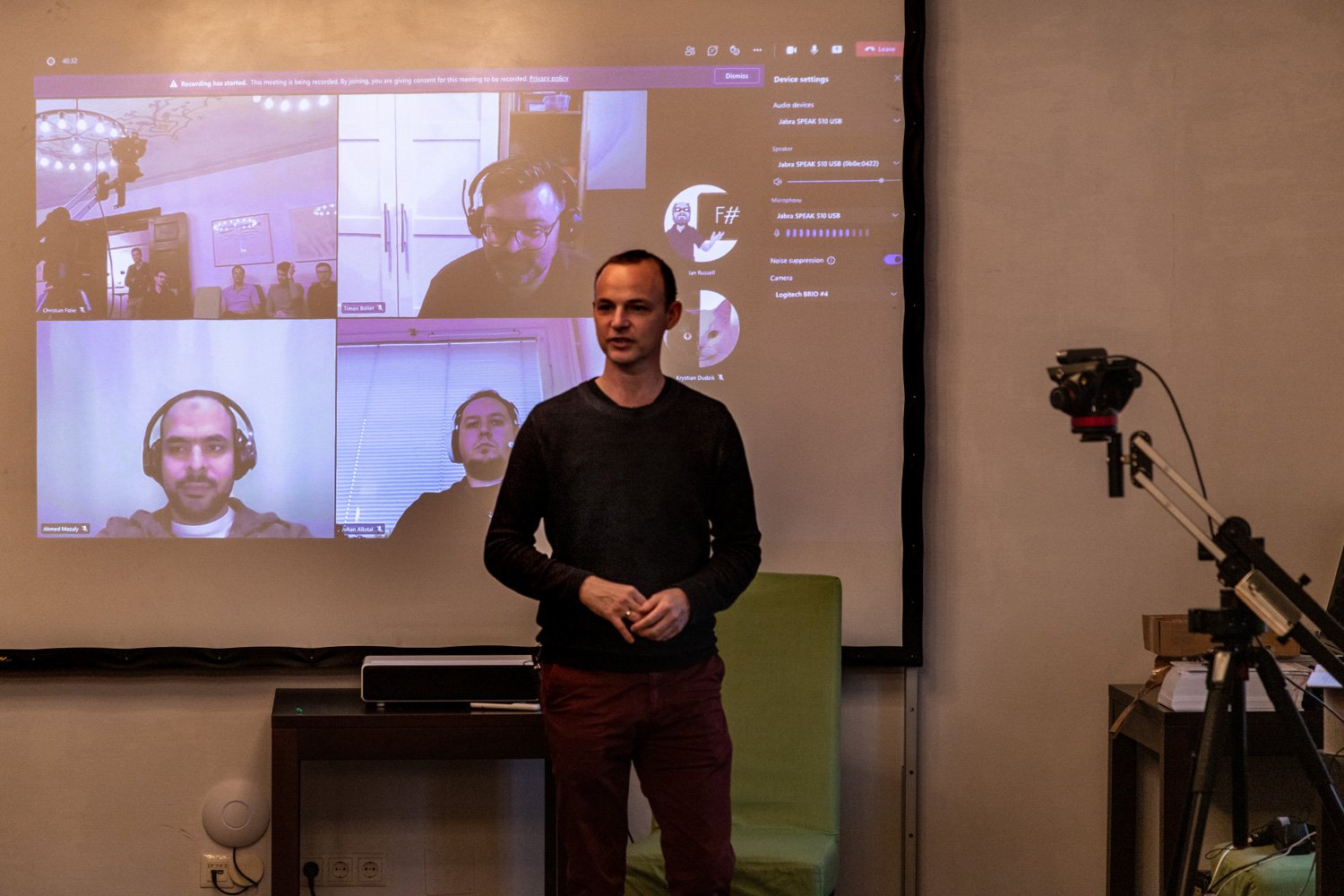 Jörg giving a presentation in a room, in front of a projection from a company video call