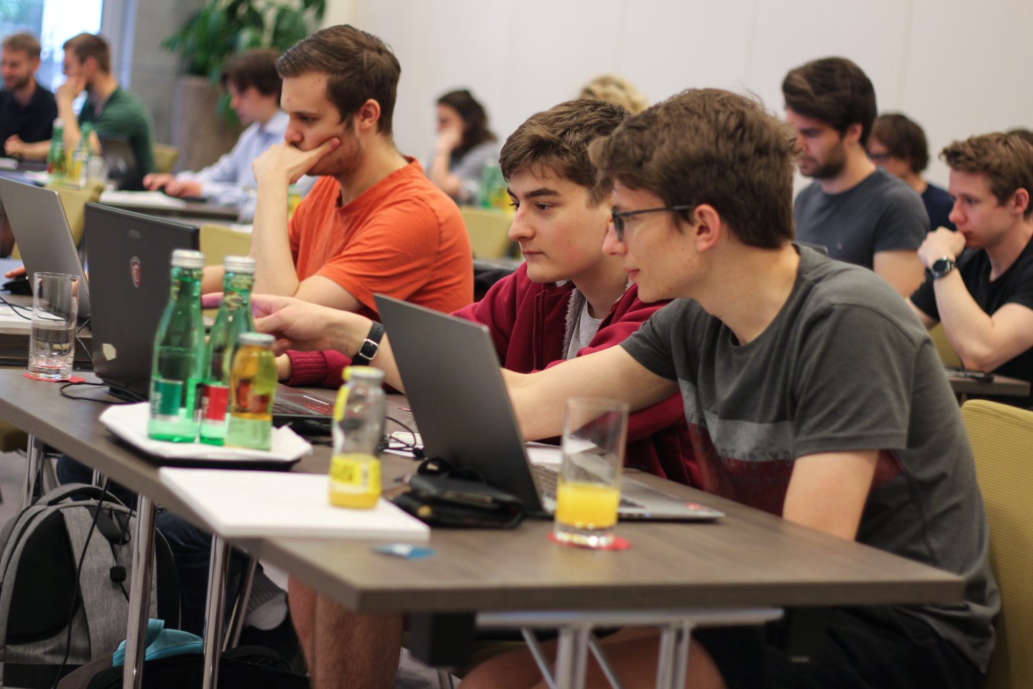 Hackathon attendees, mostly men, sitting at desks in a large room, looking concentrated at their laptop screens