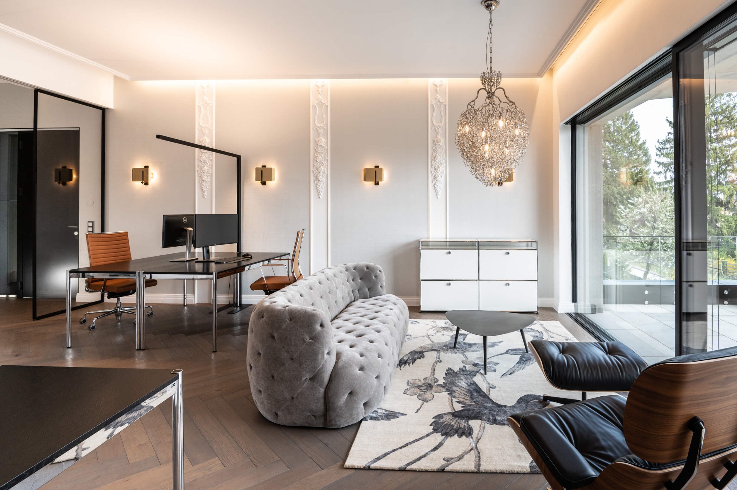 An open plan office with a soft, large couch, small table and a rug, some desks and chairs in the background and decorative moulding on the walls