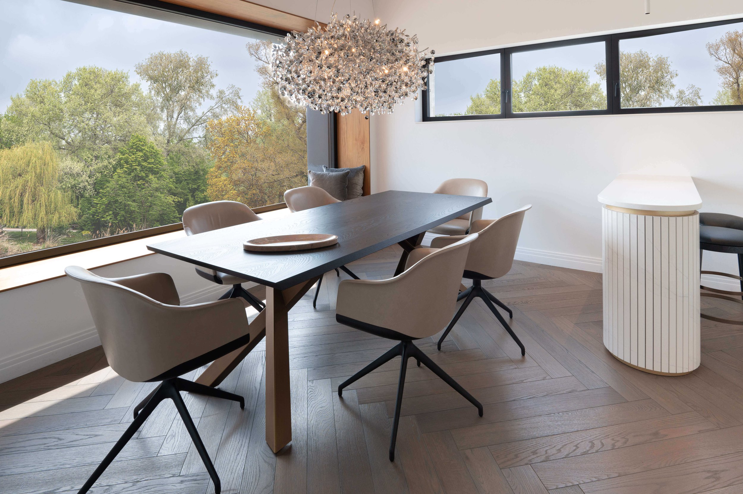 The Trustbit conference room: A clean, minimalistic table and chairs under a modern chandelier in front of a wide window overlooking trees