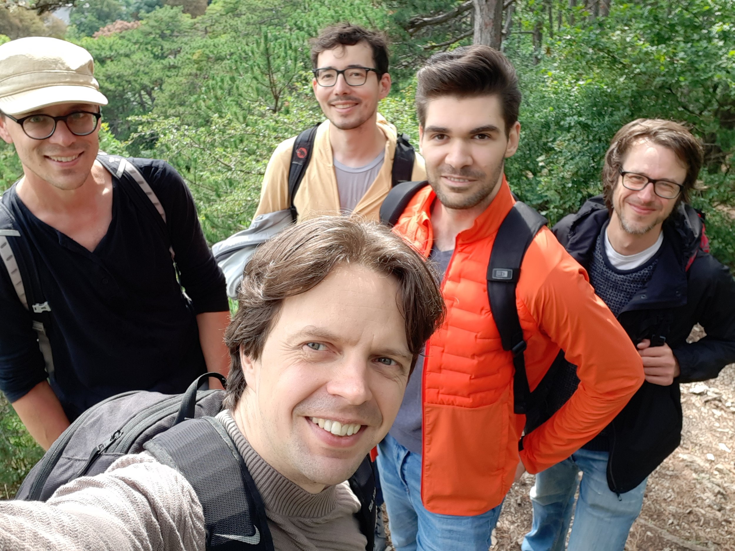 A group of Trustbit employees - Alex, Vadim, Rinat, Oscar and Daniel W - outdoors in a forest, taking a selfie during a company hike