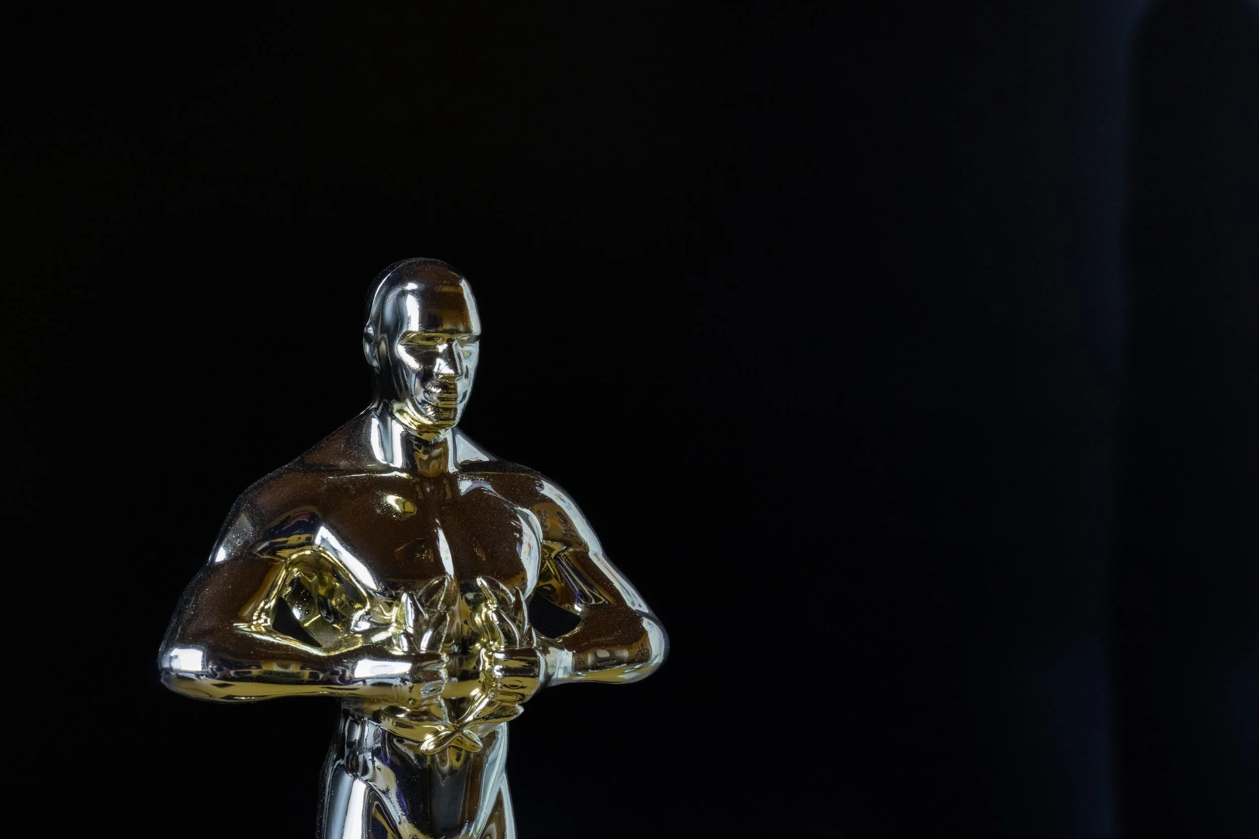 A shiny, metallic, gold-colored award or trophy resembling a human figure with a serious face, standing against a black background.