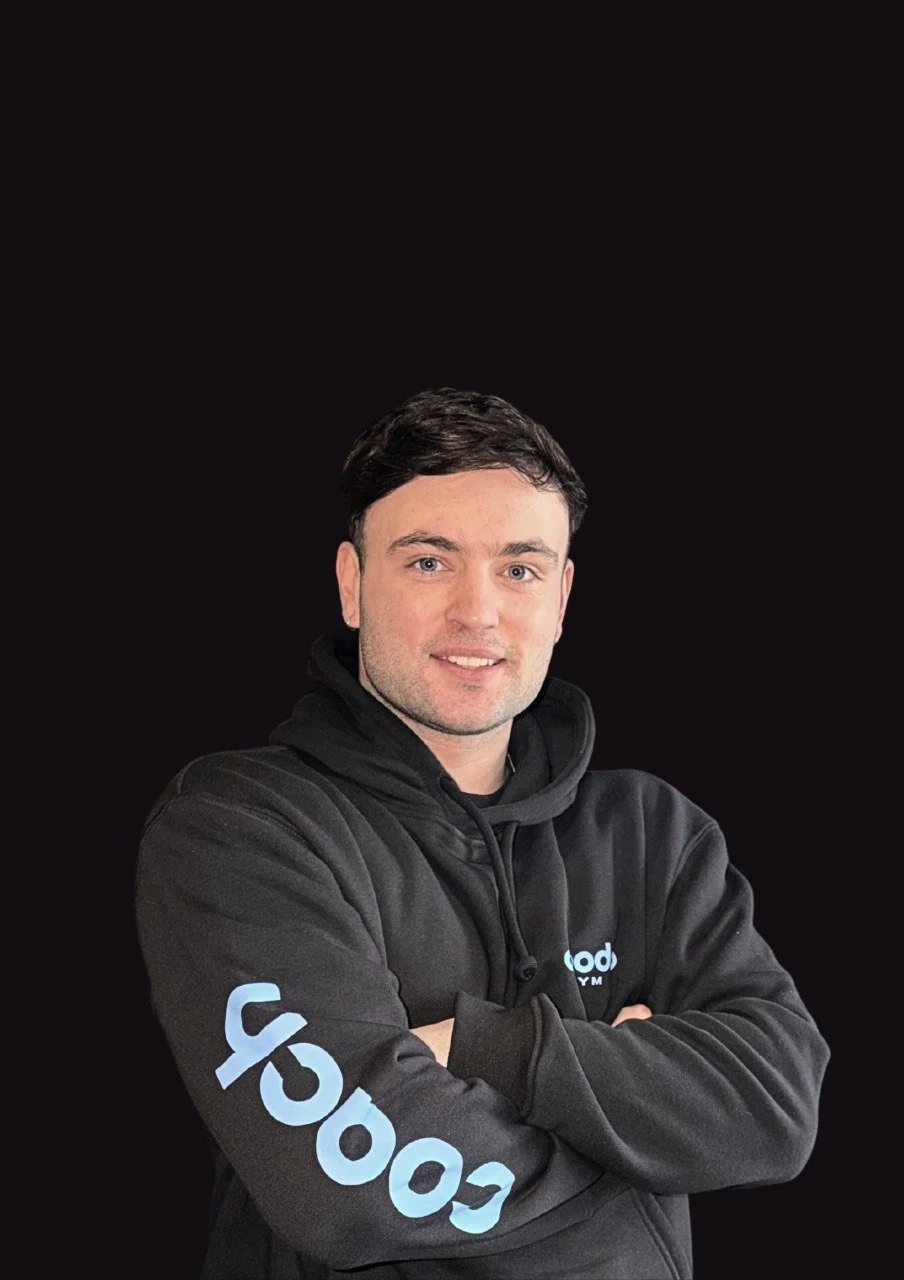 A young man with short dark hair, light skin, and blue eyes standing against a black background, wearing a black hoodie with light blue text.