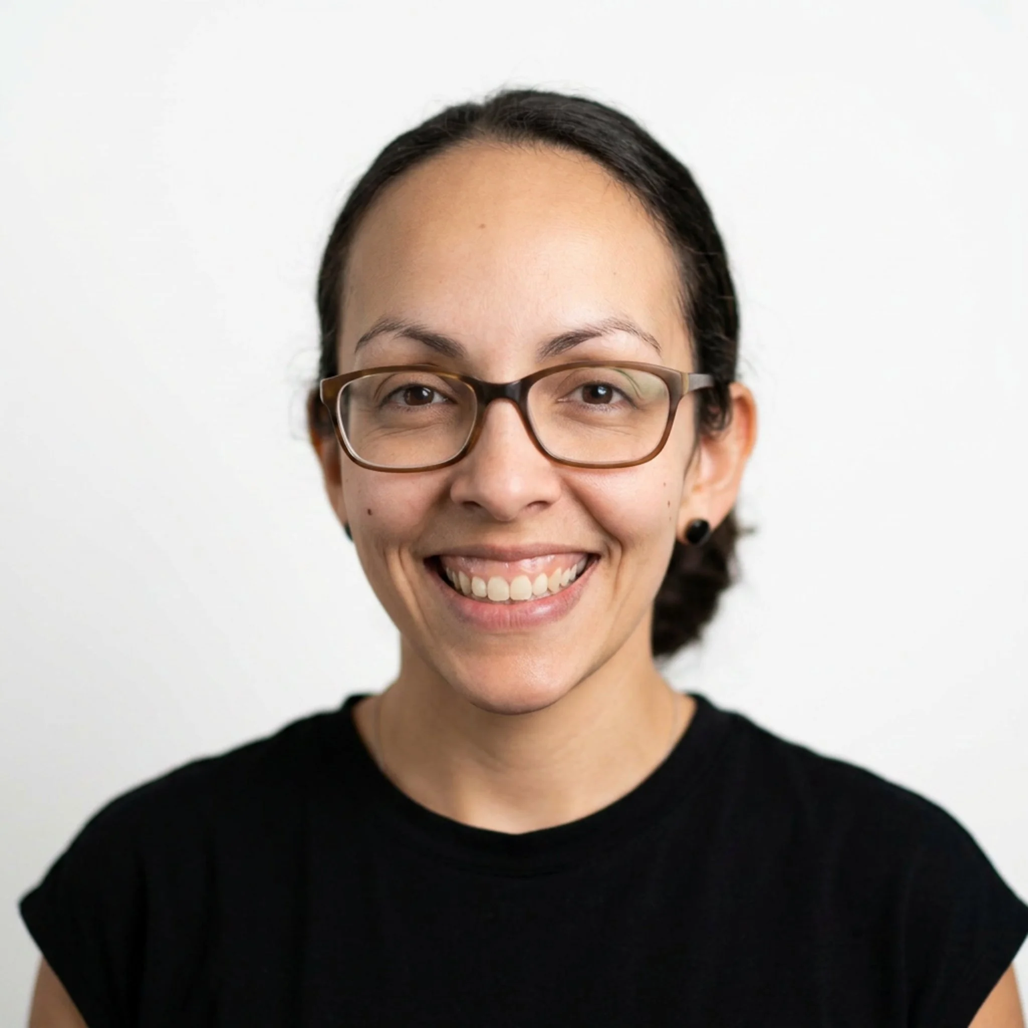 Close-up of a smiling woman's face with dark hair, wearing glasses, and a black top against a plain white background.