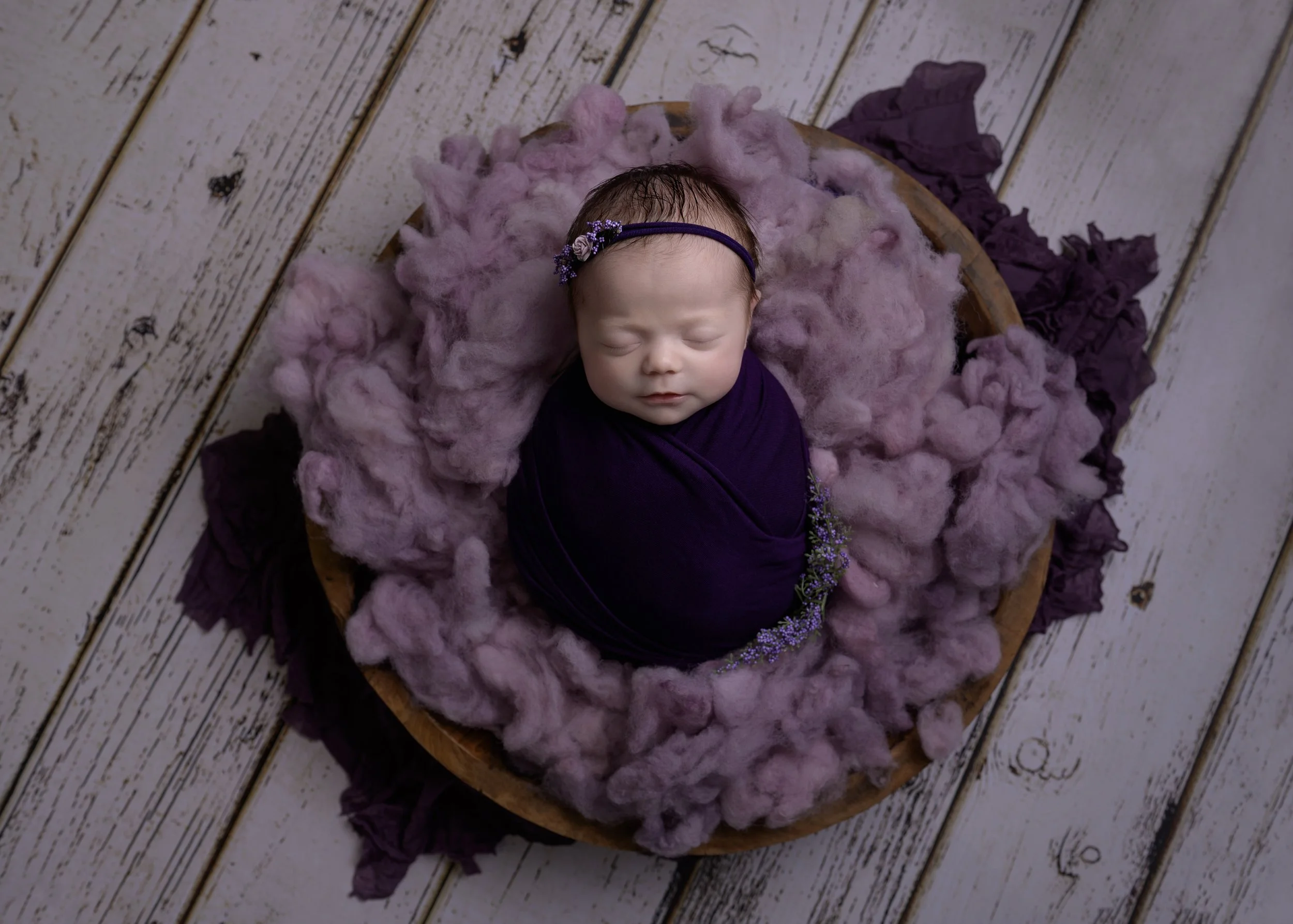 baby girl in purple asleep in a bowl by newborn photographer in Bishops Stortford
