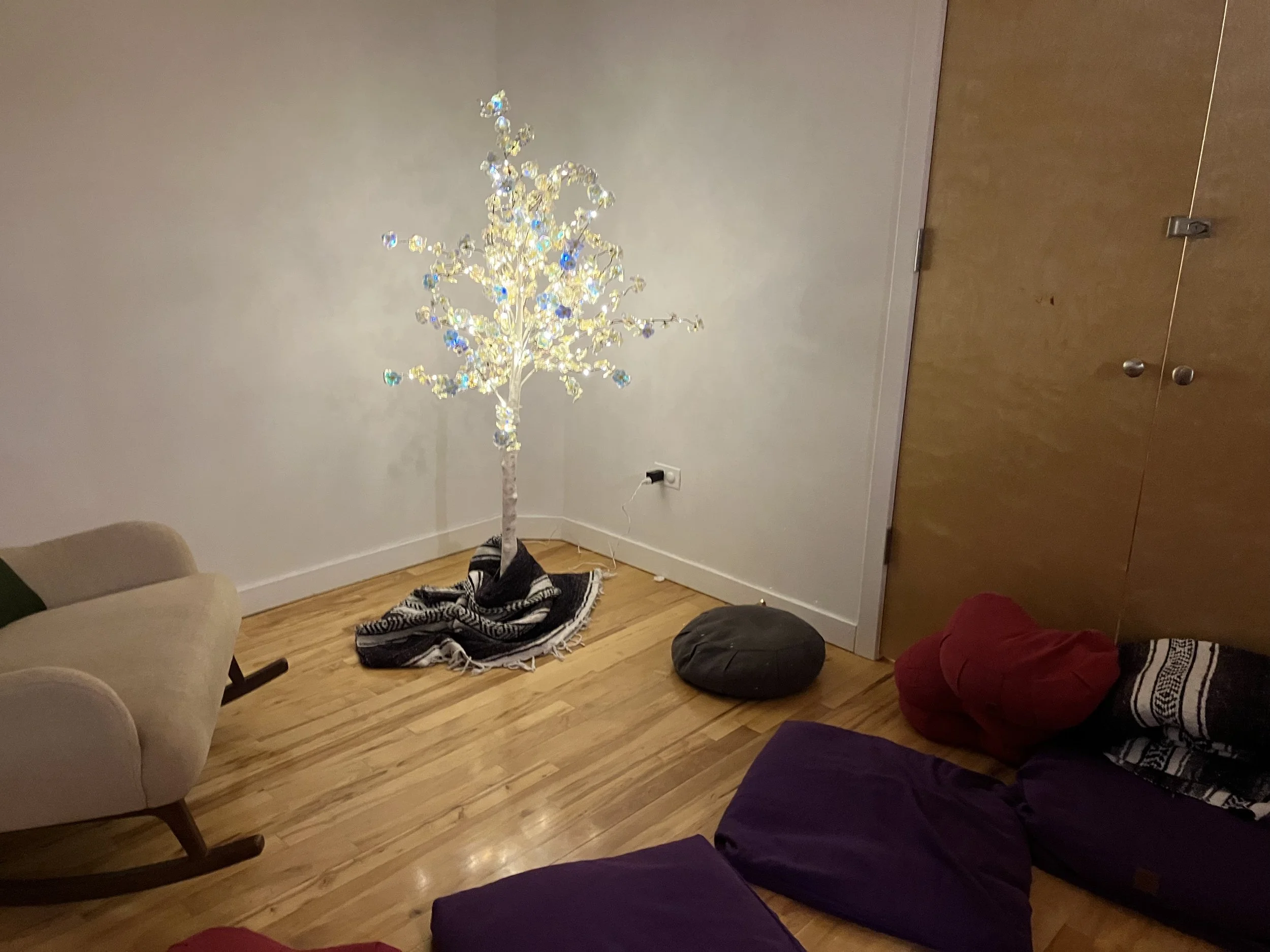 a lighted tree in the corner of a room with pillows and blanketss surrounding it