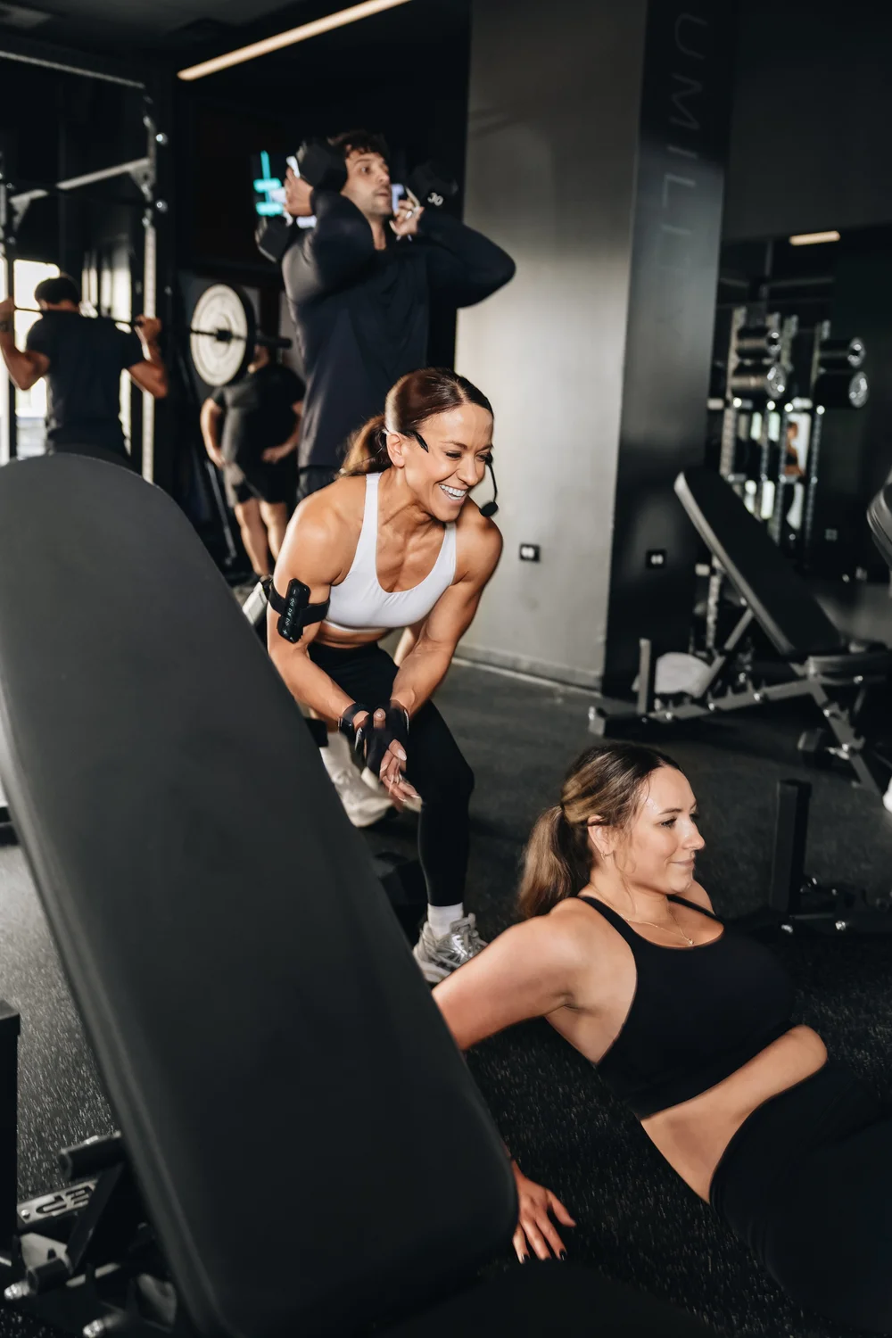 A coach wearing a headset mic leaning in to cue a client seated on the floor, others training behind them