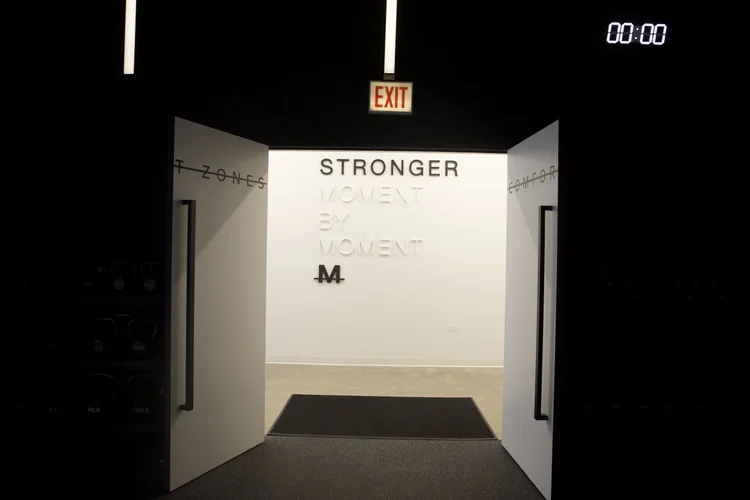 The lit white entrance into the training floor, STRONGER MOMENT BY MOMENT lettering on the far wall