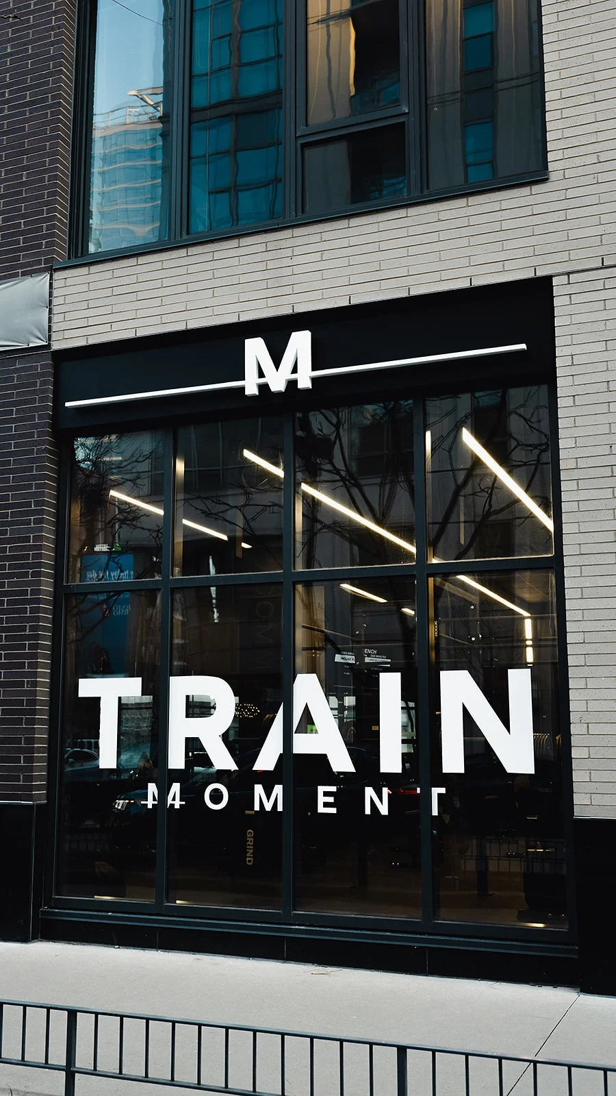 The studio storefront from the sidewalk, TRAIN MOMENT and the M mark across the black window band