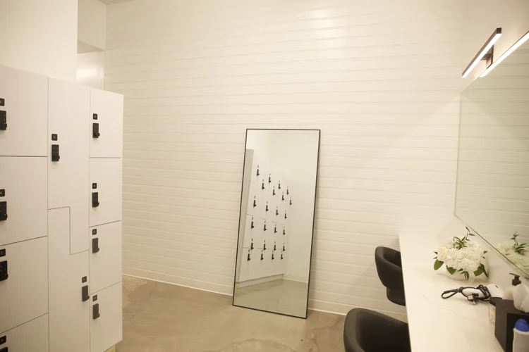 The locker room, numbered white lockers and a full-length mirror leaning against a slatted wall