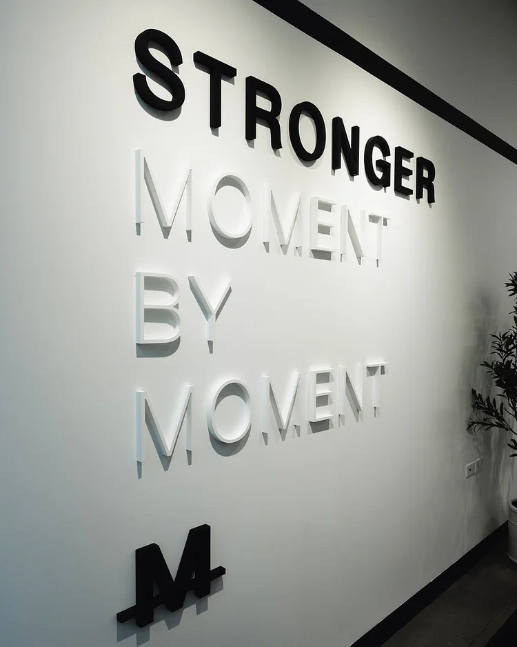 STRONGER MOMENT BY MOMENT in raised lettering on a white wall above the M mark