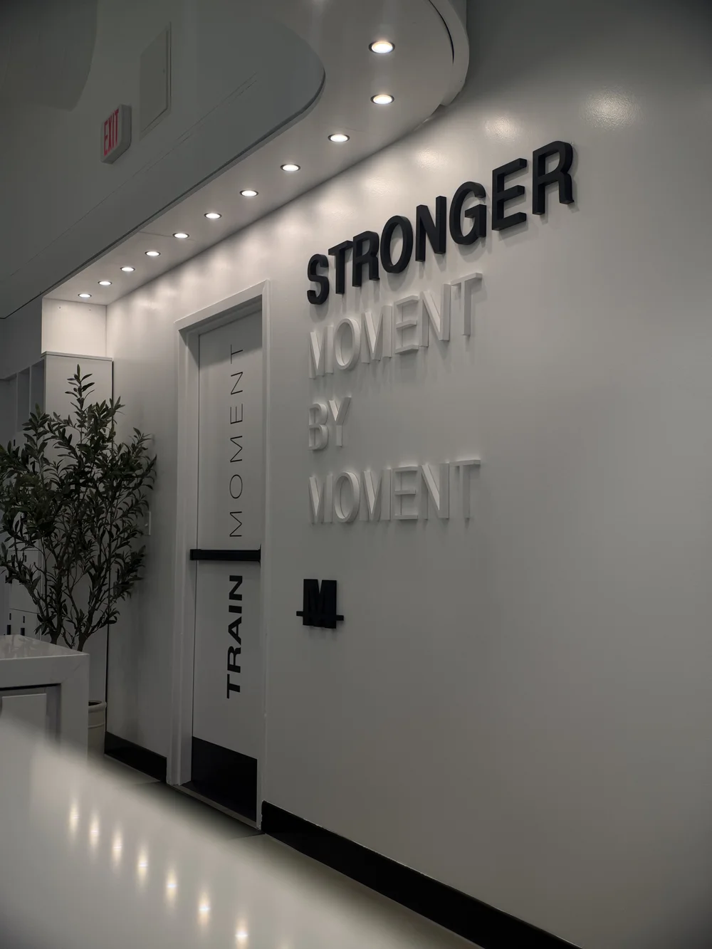 STRONGER MOMENT BY MOMENT in raised lettering on a white wall beside a TRAIN MOMENT column