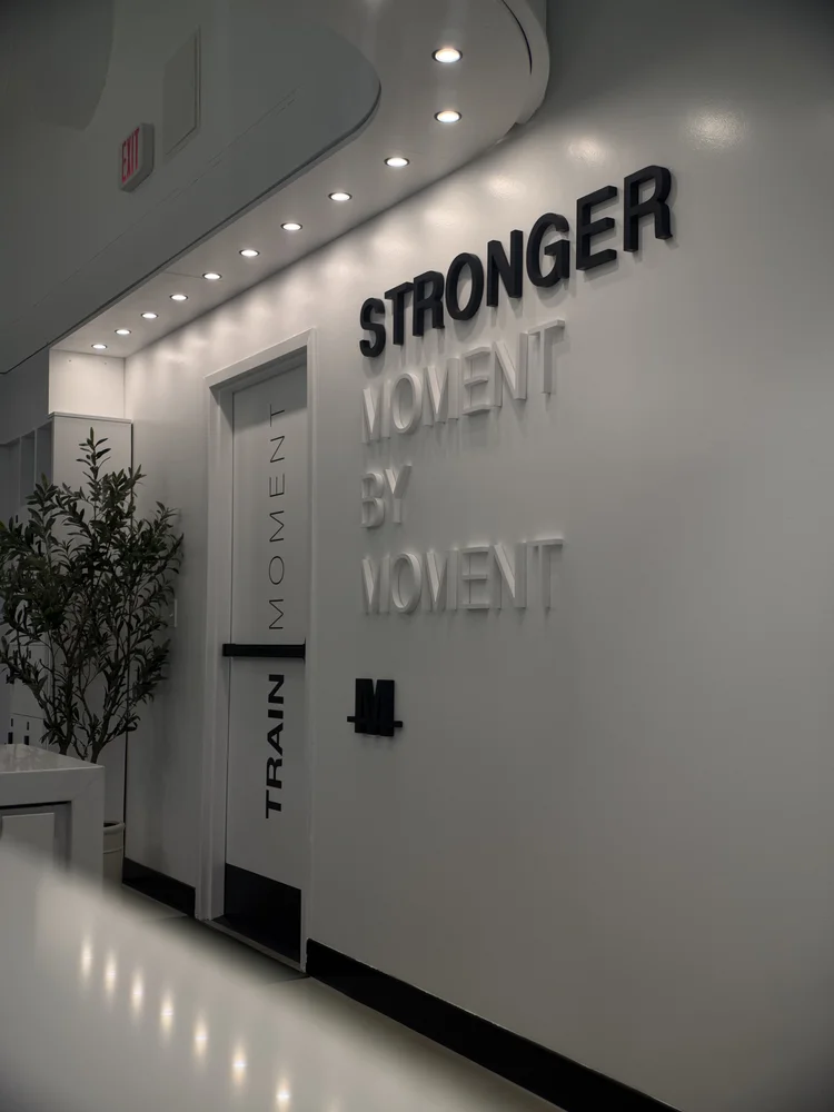 STRONGER MOMENT BY MOMENT in raised lettering on a white wall beside a TRAIN MOMENT column
