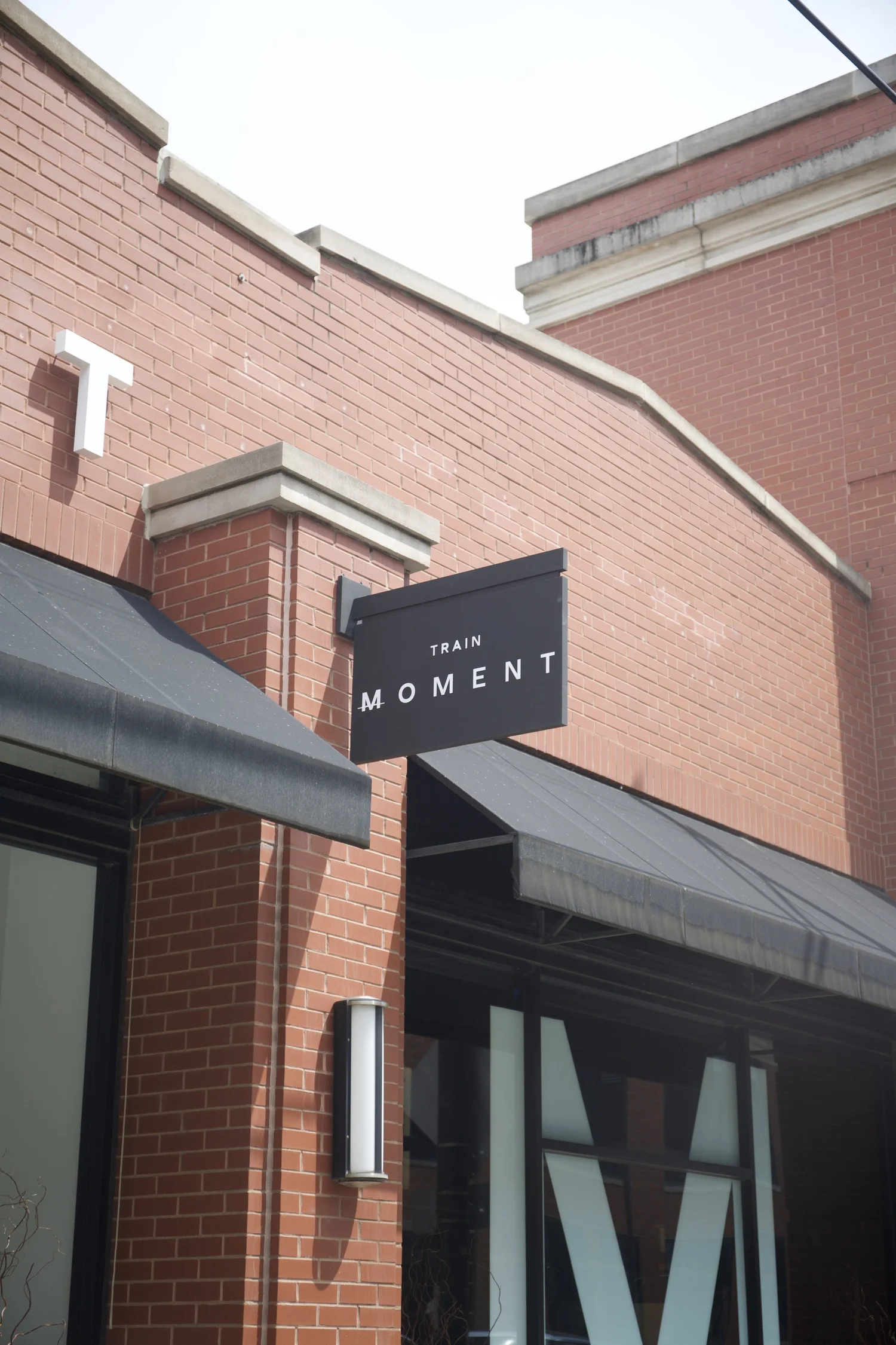 The studio's red brick facade, a black TRAIN MOMENT blade sign hanging over the awning