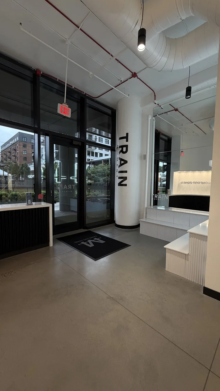 Inside the entrance, TRAIN lettering down the white column and an M floor mat between the glass doors