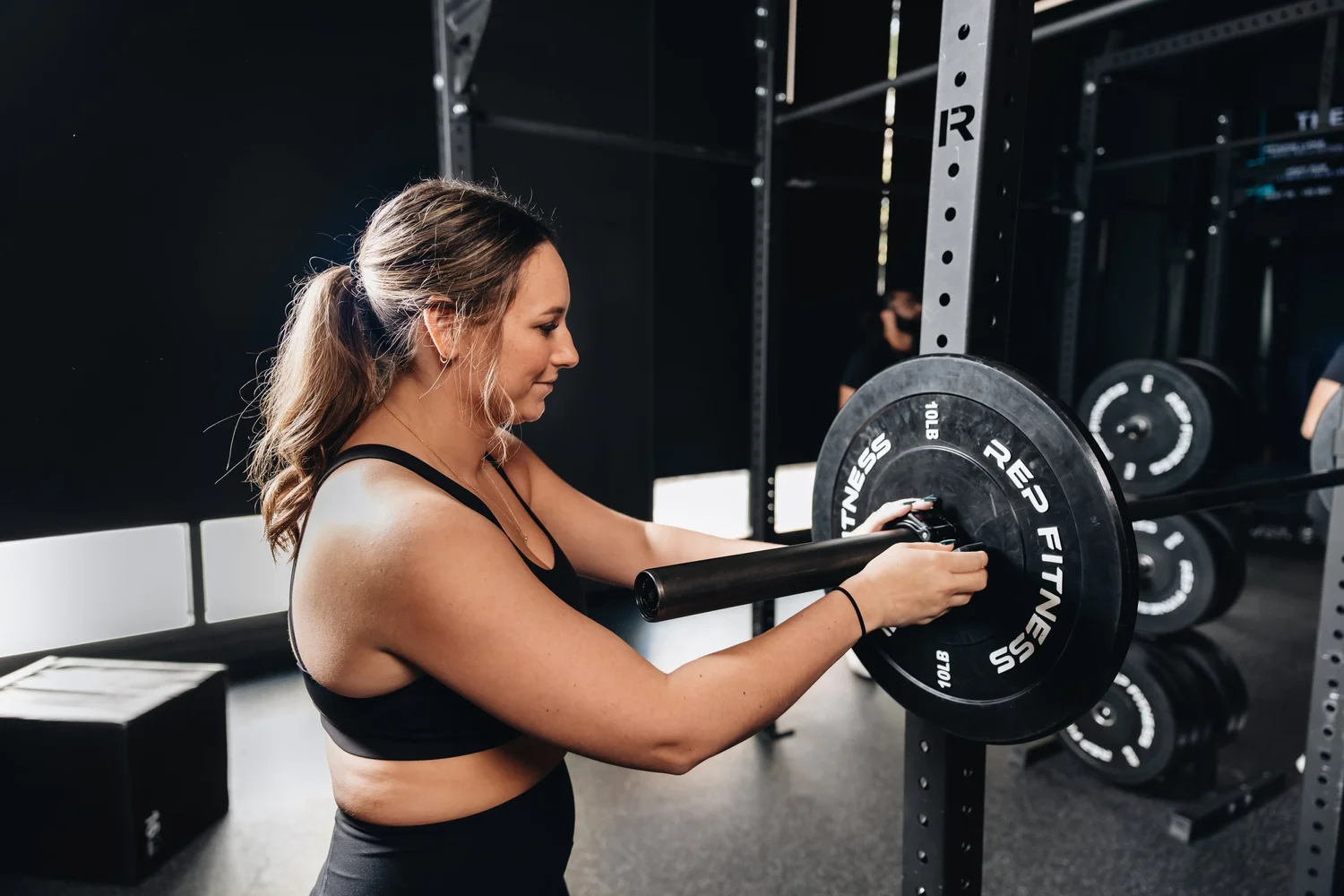 A member loading a plate onto a barbell at TRAIN Moment River North