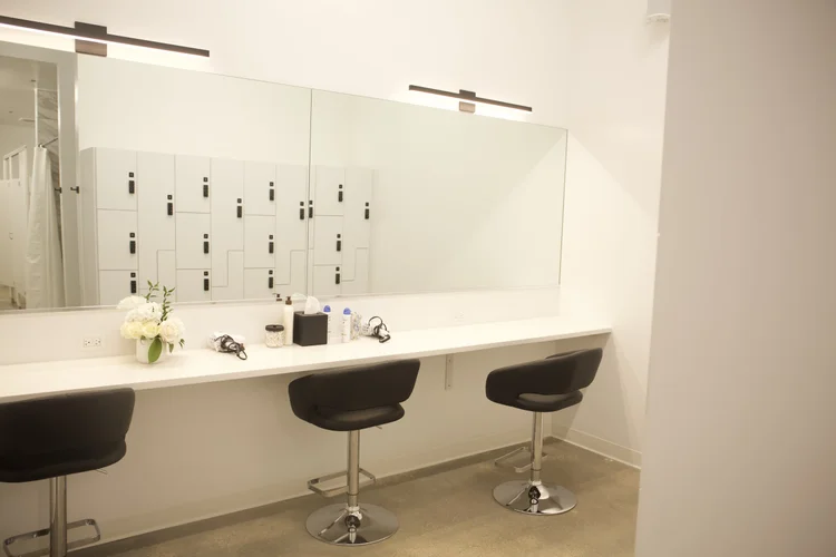 The vanity counter, a long mirror, two black stools and a vase of white flowers