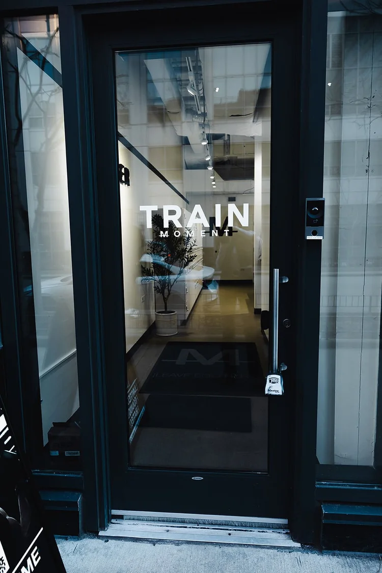 The glass entrance door with TRAIN MOMENT on it, the lit reception and the M floor mat visible inside