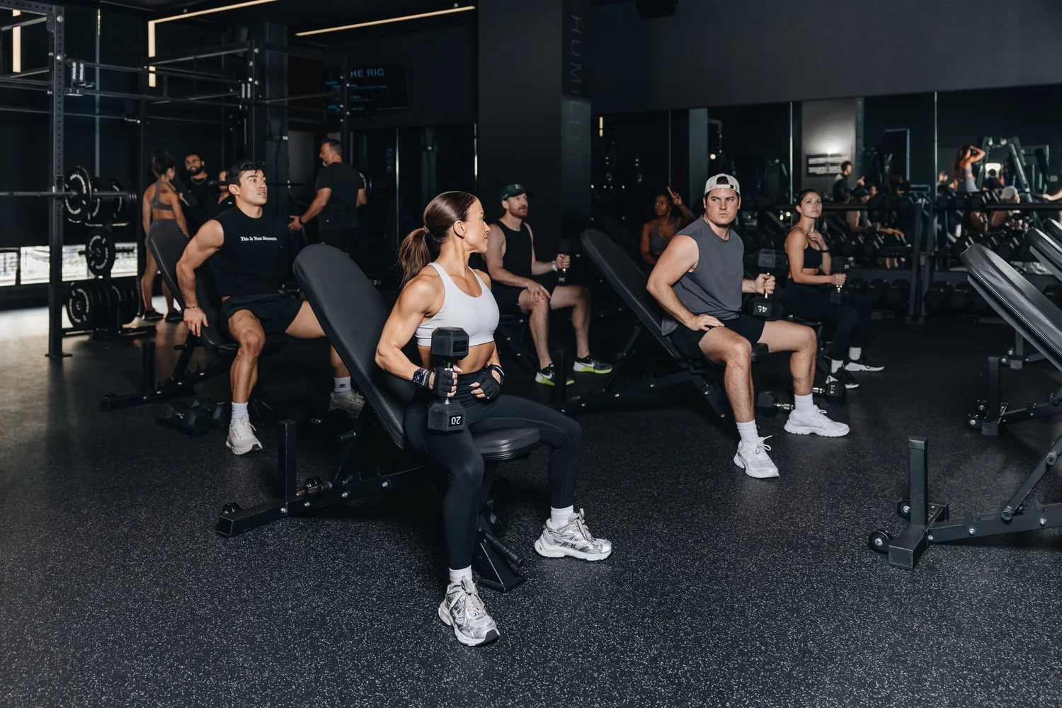 A group mid-session on incline benches, each pressing a dumbbell, the studio's rig and mirrors behind them