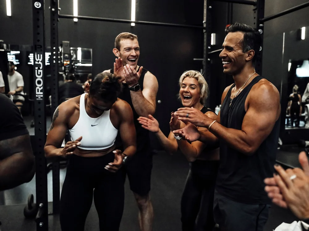 A coach and four clients smiling and applauding together on the training floor
