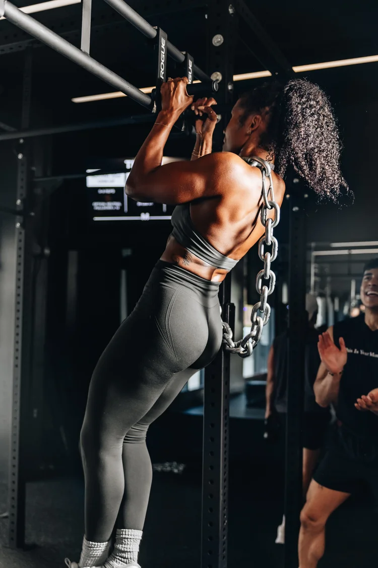 A woman seen from behind pulling a bar down with both hands, back and shoulders under load