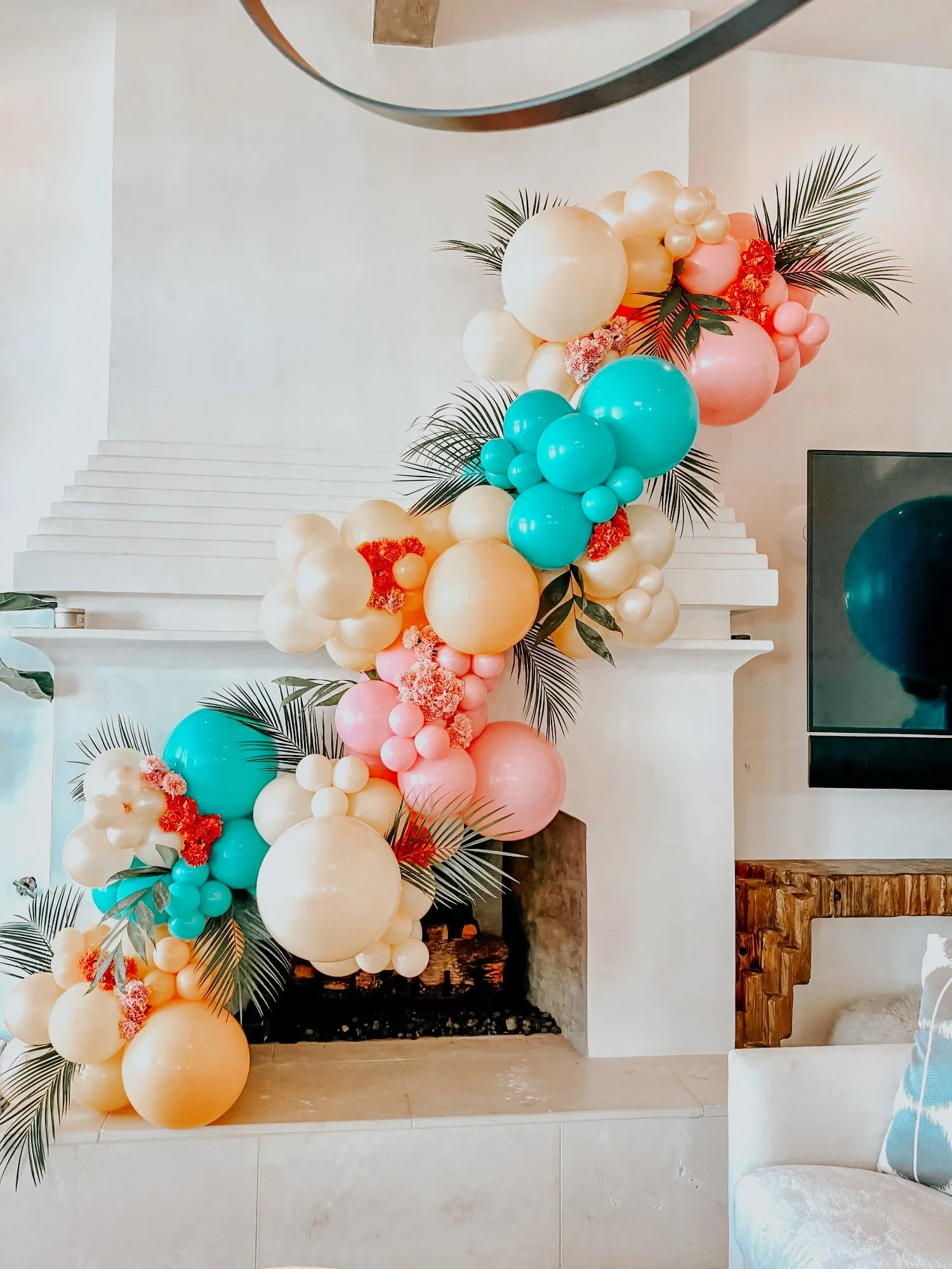 Pastel yellow, pink, blue, and cream balloon décor with palm leaves styled on a white fireplace mantle for a 30A indoor celebration.