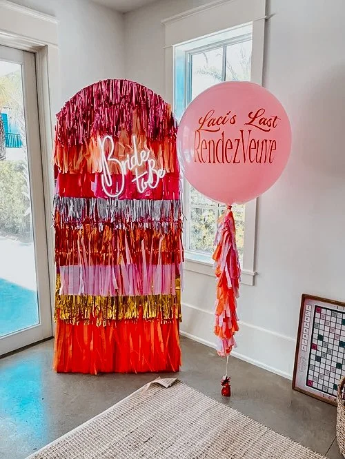 Custom bachelorette party backdrop with fringe wall and personalized balloons inside an Alys Beach vacation rental.