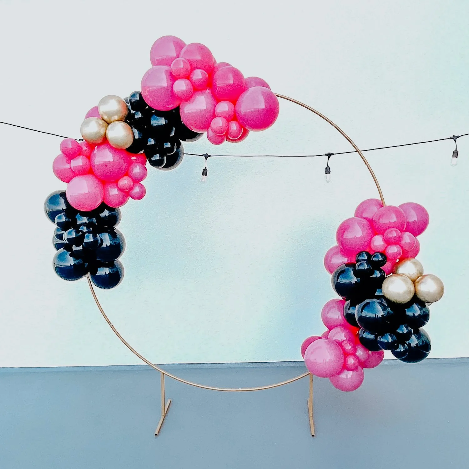 Pink, black, gold, and purple balloon décor on a gold circular ring display for a 30A indoor celebration.