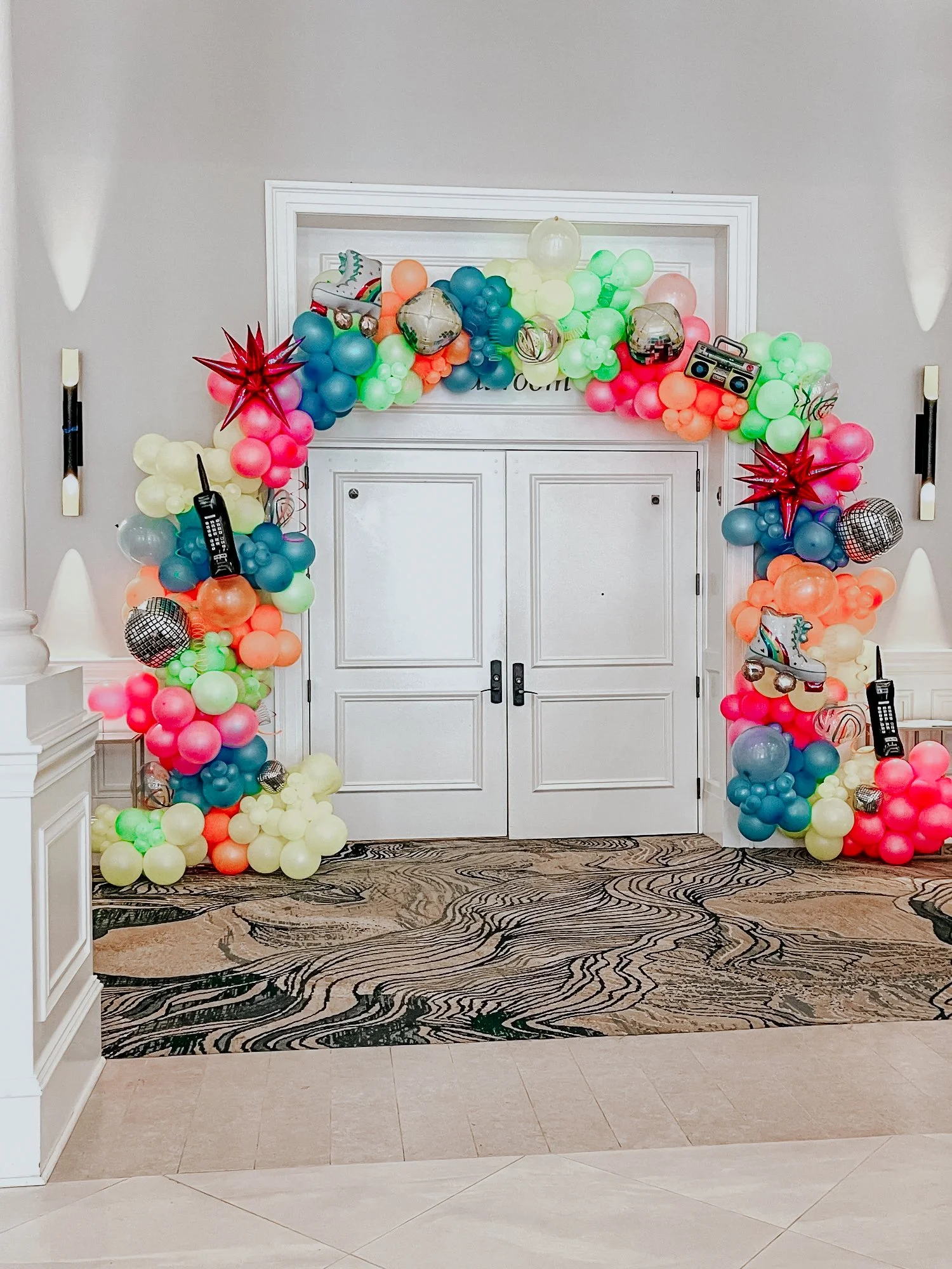 Neon balloon arch with star balloons, disco balls, toy phones, and a boombox styled around double doors for a 30A themed party.