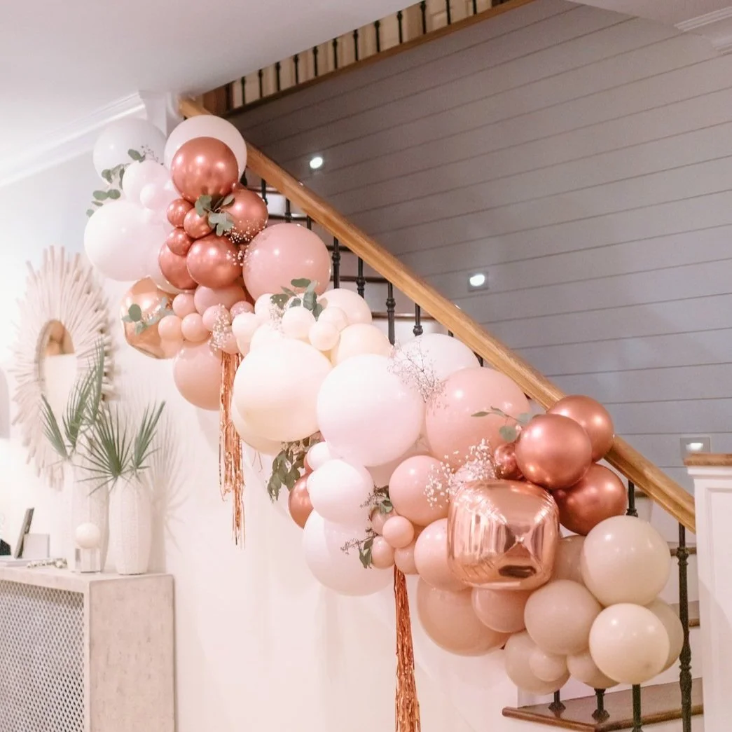 Pink, white, and rose gold balloon garland décor with greenery styled along a staircase banister for a 30A indoor event.